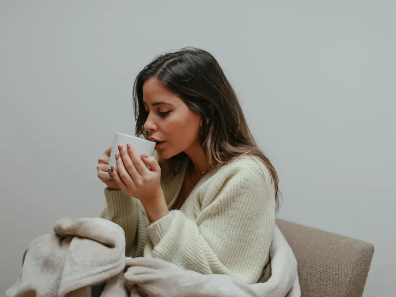 A young woman wrapped in a blanket sips a hot drink in a quiet moment