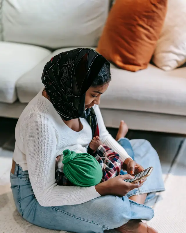 A mother sitting on the floor breastfeeds her baby discreetly under her sweater