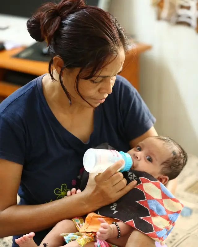 A mother gives a bottle to her young baby held in her arms